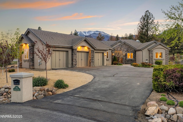 193 N Argyle Ct, Reno, NV 89511 - view of front facade featuring stone siding, an attached garage, driveway, a tiled roof, and a mountain view