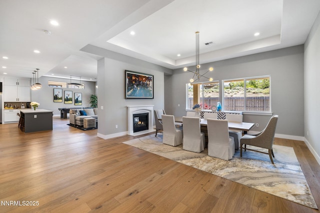 3060 Feathertop Dr, Reno, NV 89521 - dining room featuring a raised ceiling, light wood-style floors, recessed lighting, baseboards, and a glass covered fireplace