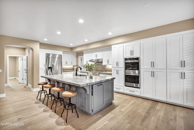 2965 Roundrock Ct, Reno, NV 89511 - kitchen with stainless steel appliances, under cabinet range hood, arched walkways, baseboards, and light wood-style floors