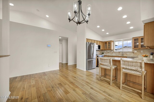 1458 Rosy Finch Dr, Sparks, NV 89441 - kitchen featuring appliances with stainless steel finishes, brown cabinetry, lofted ceiling, light wood finished floors, and light stone counters