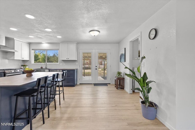 1235 Koontz Ln, Carson City, NV 89701 - kitchen featuring a textured ceiling, a kitchen bar, white cabinetry, wall chimney exhaust hood, and light wood finished floors