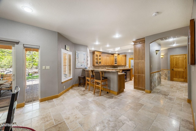 14501 Quail Rock Ct, Reno, NV 89511 - kitchen featuring a peninsula, glass insert cabinets, light stone counters, a breakfast bar, and arched walkways