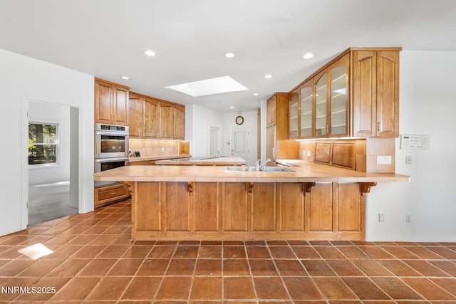 390 Sylvan Ct, Verdi, NV 89439 - kitchen featuring a skylight, stainless steel double oven, a sink, glass insert cabinets, and a peninsula