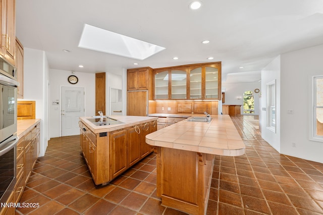 390 Sylvan Ct, Verdi, NV 89439 - kitchen featuring a skylight, an island with sink, a sink, tile counters, and glass insert cabinets