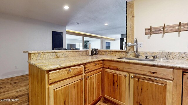 5895 Brooke Dr, Winnemucca, NV 89445 - kitchen with light wood-type flooring, a sink, light stone countertops, a peninsula, and baseboards