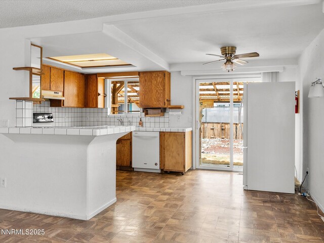 1344 Patricia Dr, Gardnerville, NV 89460 - kitchen with white appliances, tile counters, brown cabinetry, under cabinet range hood, and a ceiling fan