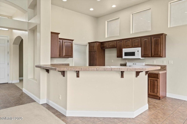 1239 Flintwood Dr, Carson City, NV 89703 - kitchen featuring white microwave, arched walkways, light tile patterned flooring, a breakfast bar, and recessed lighting