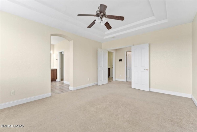1239 Flintwood Dr, Carson City, NV 89703 - unfurnished bedroom featuring light carpet, arched walkways, a tray ceiling, and baseboards