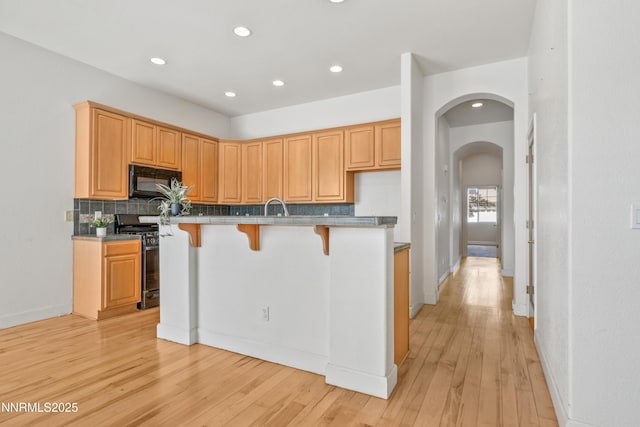 6638 Aston Cir, Sparks, NV 89436 - kitchen with range with gas cooktop, black microwave, arched walkways, decorative backsplash, and light wood-type flooring