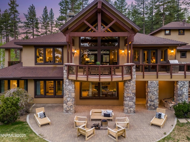 235 Timbercreek Ct, Reno, NV 89511 - back of property at dusk with stucco siding, a patio area, a shingled roof, a balcony, and an outdoor hangout area