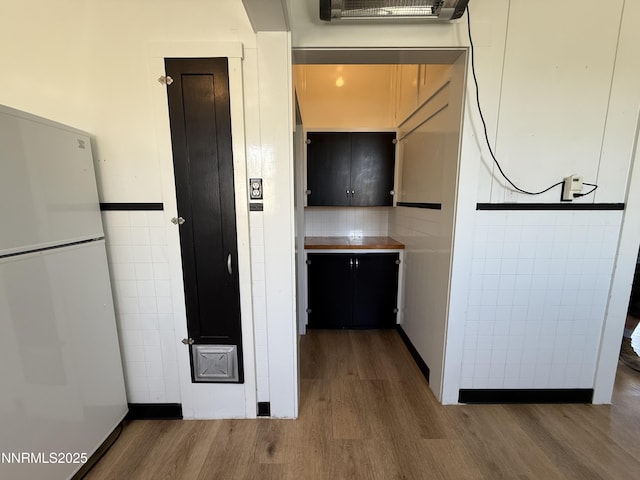 141 University St, Tonopah, NV 89049 - kitchen with wood finished floors, freestanding refrigerator, tile walls, dark cabinetry, and backsplash