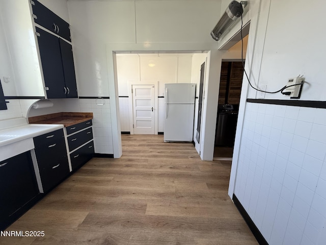141 University St, Tonopah, NV 89049 - kitchen featuring freestanding refrigerator, tile walls, dark cabinetry, light wood-style floors, and stove