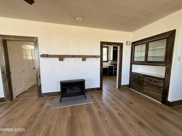 141 University St, Tonopah, NV 89049 - unfurnished living room with wood finished floors, a wood stove, baseboards, wood walls, and a sink