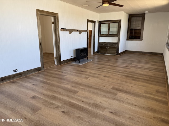 141 University St, Tonopah, NV 89049 - unfurnished living room featuring a wood stove, a ceiling fan, baseboards, and wood finished floors