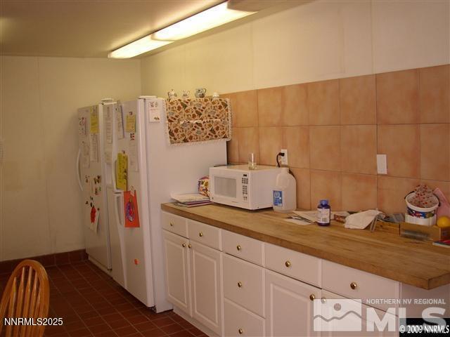 11000 Mount Rose Hwy, Reno, NV 89511 - kitchen featuring white microwave, butcher block countertops, white cabinets, dark tile patterned floors, and tile walls