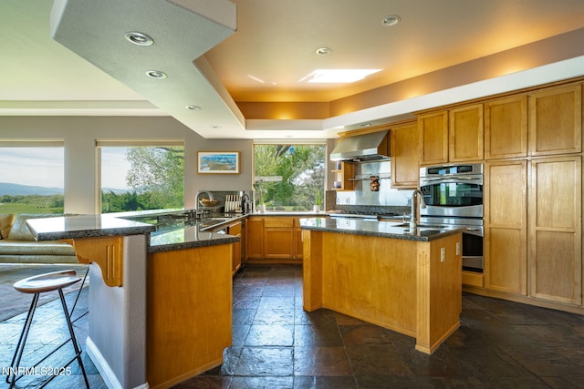 2473 Genoa Aspen Dr, Genoa, NV 89411 - kitchen featuring wall chimney exhaust hood, double oven, stone tile floors, a peninsula, and dark stone counters