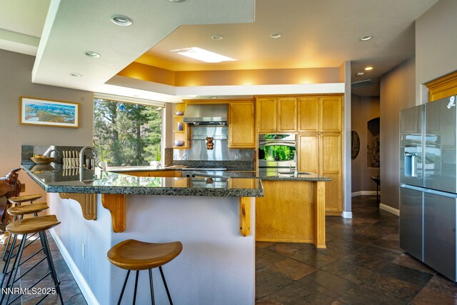 2473 Genoa Aspen Dr, Genoa, NV 89411 - kitchen featuring stainless steel fridge, a peninsula, a kitchen breakfast bar, wall chimney range hood, and dark stone counters