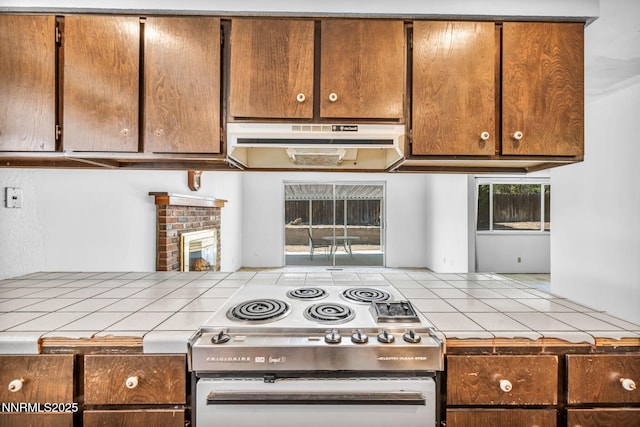 1129 Sonoma St, Carson City, NV 89701 - kitchen featuring tile countertops, stove, under cabinet range hood, brown cabinets, and a brick fireplace