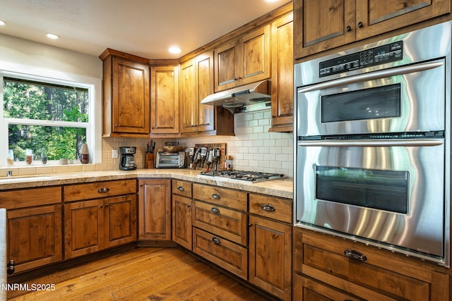 625 Freel Dr, Zephyr Cove, NV 89448 - kitchen with appliances with stainless steel finishes, brown cabinetry, wood finished floors, under cabinet range hood, and light countertops