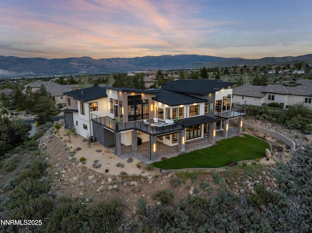 3041 Palmer Pointe Ct, Reno, NV 89511 - back of house at dusk with an attached garage, stucco siding, a lawn, and a deck with mountain view
