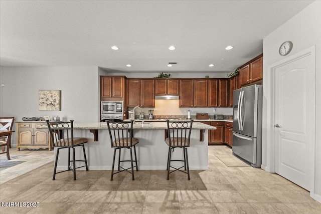 2269 Isabella Ct, Sparks, NV 89434 - kitchen with appliances with stainless steel finishes, light stone counters, an island with sink, under cabinet range hood, and a breakfast bar