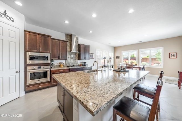 332 Blooming Sage Way, Spanish Springs, NV 89441 - kitchen with stainless steel appliances, wall chimney exhaust hood, light stone countertops, a breakfast bar area, and an island with sink
