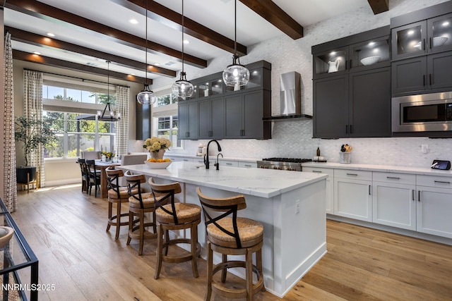 208 Criollo Ct, Reno, NV 89511 - kitchen featuring stainless steel microwave, wall chimney exhaust hood, light wood finished floors, tasteful backsplash, and an island with sink