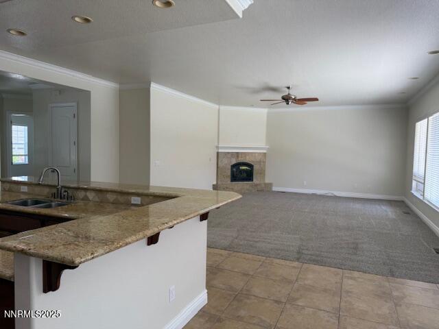 1313 Cedar Creek Cir, Gardnerville, NV 89460 - kitchen with light carpet, ceiling fan, a breakfast bar area, light stone counters, and a tile fireplace