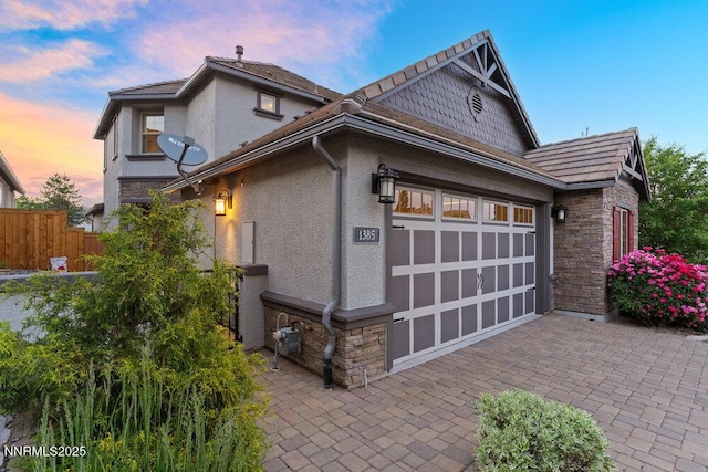 1385 Balfour Dr, Reno, NV 89509 - property exterior at dusk with stone siding, a garage, stucco siding, and decorative driveway