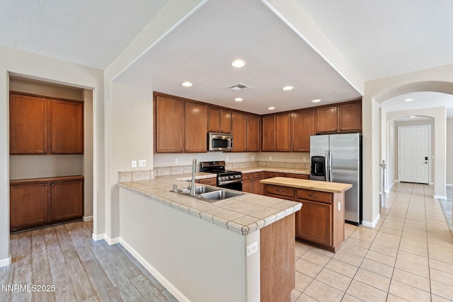 7121 Jermann Dr, Sparks, NV 89436 - kitchen featuring stainless steel appliances, arched walkways, a peninsula, brown cabinetry, and recessed lighting