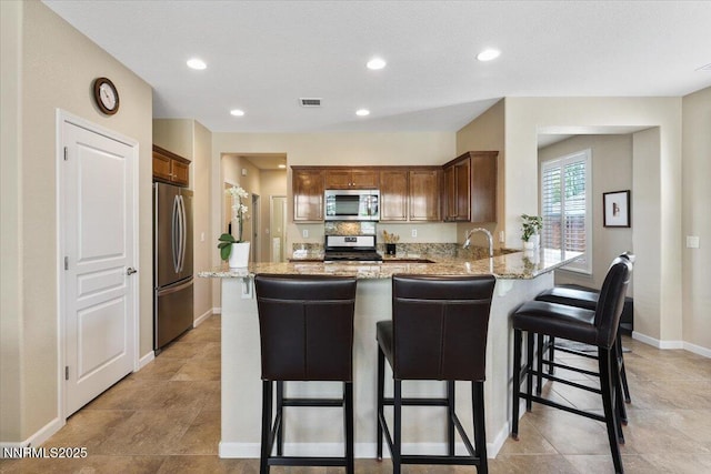 1605 W Del Webb Pkwy, Reno, NV 89523 - kitchen featuring stainless steel appliances, a peninsula, light stone counters, a breakfast bar area, and baseboards