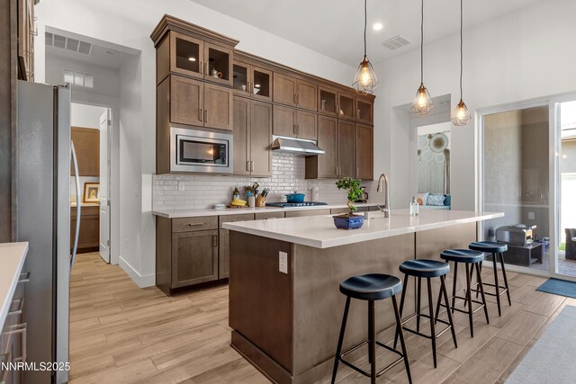 611 Camargue Trl, Reno, NV 89511 - kitchen featuring appliances with stainless steel finishes, under cabinet range hood, light wood-type flooring, light countertops, and a kitchen bar