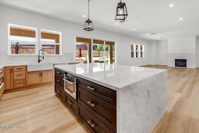 9740 Cardigan Bay Ln, Reno, NV 89521 - kitchen with recessed lighting, light stone counters, light wood-style flooring, hanging light fixtures, and a glass covered fireplace