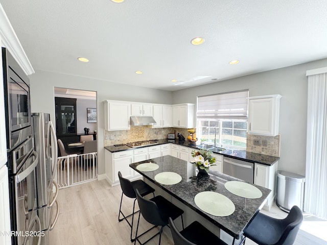 6726 Runnymede Dr, Sparks, NV 89436 - kitchen with under cabinet range hood, appliances with stainless steel finishes, light wood-style flooring, white cabinets, and recessed lighting