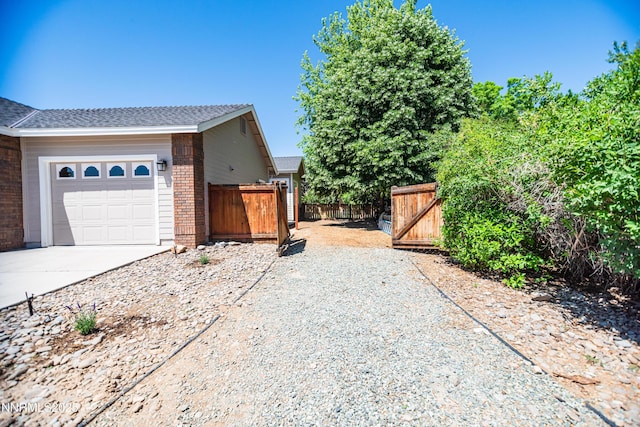 867 Mahogany Dr, Minden, NV 89423 - view of side of home with brick siding, driveway, an attached garage, a gate, and roof with shingles
