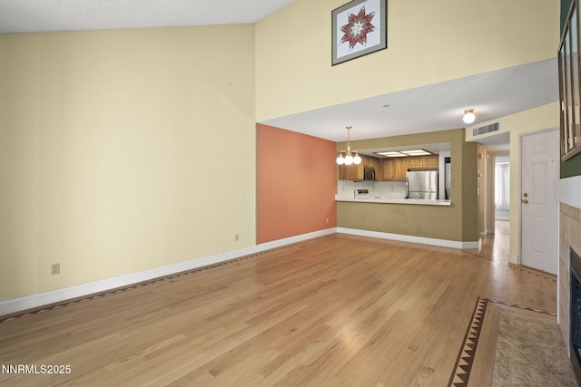 2875 Idlewild Dr Unit 106, Reno, NV 89509 - unfurnished living room featuring a chandelier, light wood finished floors, a tiled fireplace, baseboards, and a high ceiling