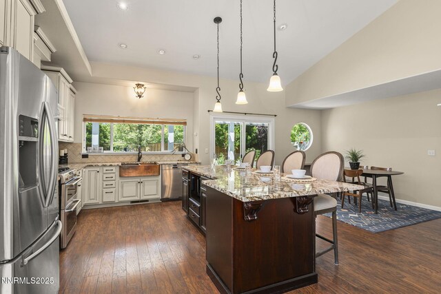 9783 Northrup Dr, Reno, NV 89521 - kitchen with appliances with stainless steel finishes, dark wood-style floors, decorative backsplash, a breakfast bar area, and light stone counters