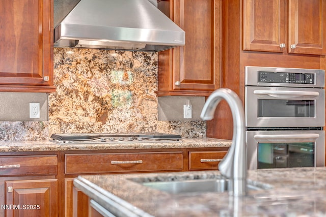 4215 Wild Eagle Ter, Reno, NV 89511 - kitchen with wall chimney range hood, stainless steel appliances, backsplash, light stone counters, and brown cabinets