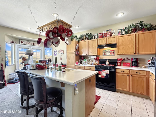 8490 Coral Reef Dr, Reno, NV 89506 - kitchen featuring black range with gas cooktop, a sink, light countertops, under cabinet range hood, and a breakfast bar