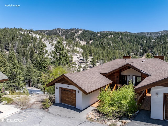 1314 Saint Gallen Ct, Incline Village, NV 89451 - view of front of home featuring a wooded view, a garage, roof with shingles, a mountain view, and stucco siding
