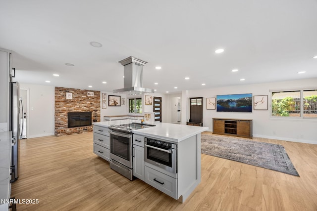 1901 S Marsh Ave, Reno, NV 89509 - kitchen with stainless steel appliances, open floor plan, a fireplace, island range hood, and light wood-style flooring