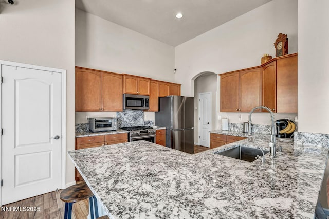 1771 Walnut Dr, Fernley, NV 89408 - kitchen with appliances with stainless steel finishes, a high ceiling, a peninsula, light stone countertops, and brown cabinets