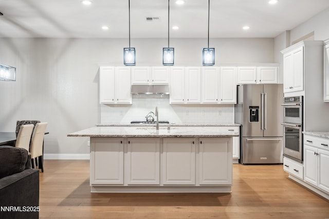 15058 Iron River Dr, Reno, NV 89521 - kitchen with appliances with stainless steel finishes, under cabinet range hood, light wood-style floors, tasteful backsplash, and white cabinets