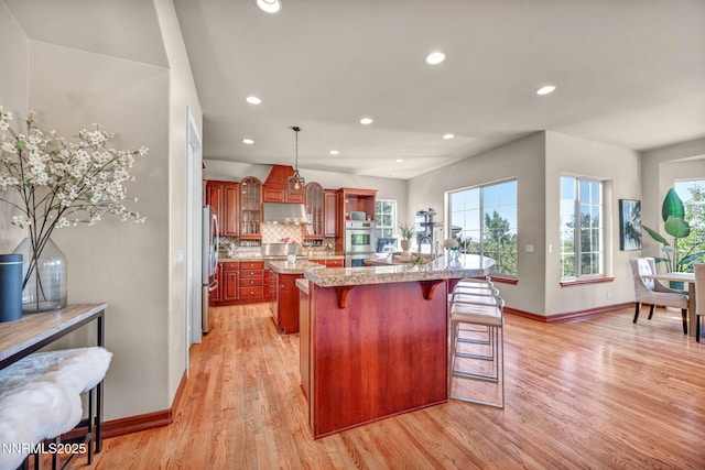 14210 Wild Quail Ct, Reno, NV 89511 - kitchen featuring appliances with stainless steel finishes, a kitchen bar, light wood-style flooring, backsplash, and under cabinet range hood