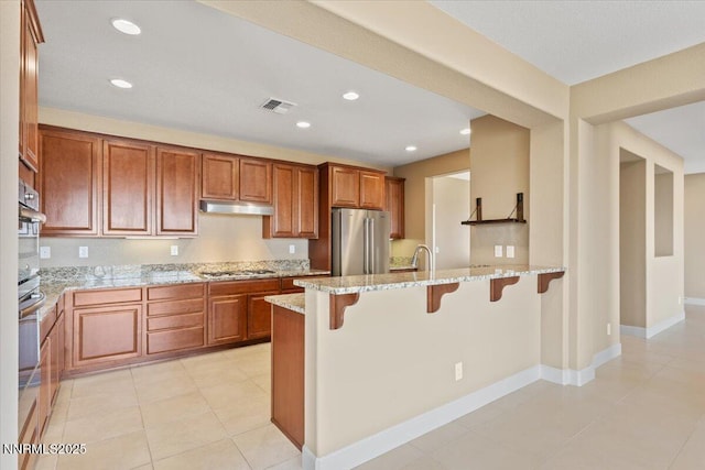 1080 S University Park Loop, Reno, NV 89512 - kitchen featuring freestanding refrigerator, under cabinet range hood, a breakfast bar, light stone counters, and a peninsula