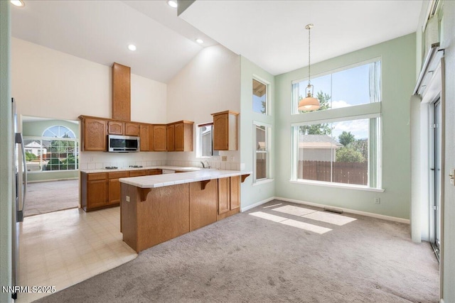 1290 Saddlehorn Ct, Minden, NV 89423 - kitchen with stainless steel microwave, high vaulted ceiling, light carpet, a peninsula, and brown cabinetry