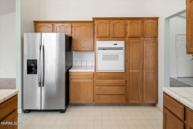 1290 Saddlehorn Ct, Minden, NV 89423 - kitchen featuring stainless steel refrigerator with ice dispenser, white oven, tile counters, and light flooring