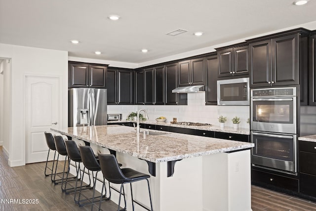 10450 Palladium Mine Dr, Reno, NV 89521 - kitchen featuring stainless steel appliances, dark wood finished floors, a kitchen island with sink, light stone countertops, and backsplash