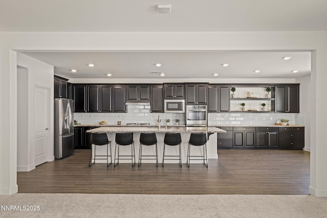 10450 Palladium Mine Dr, Reno, NV 89521 - kitchen featuring stainless steel appliances, open shelves, a kitchen island with sink, decorative backsplash, and a kitchen bar