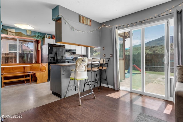 7090 Peppermint Dr, Reno, NV 89506 - kitchen with electric range, under cabinet range hood, a peninsula, a kitchen bar, and black fridge with ice dispenser